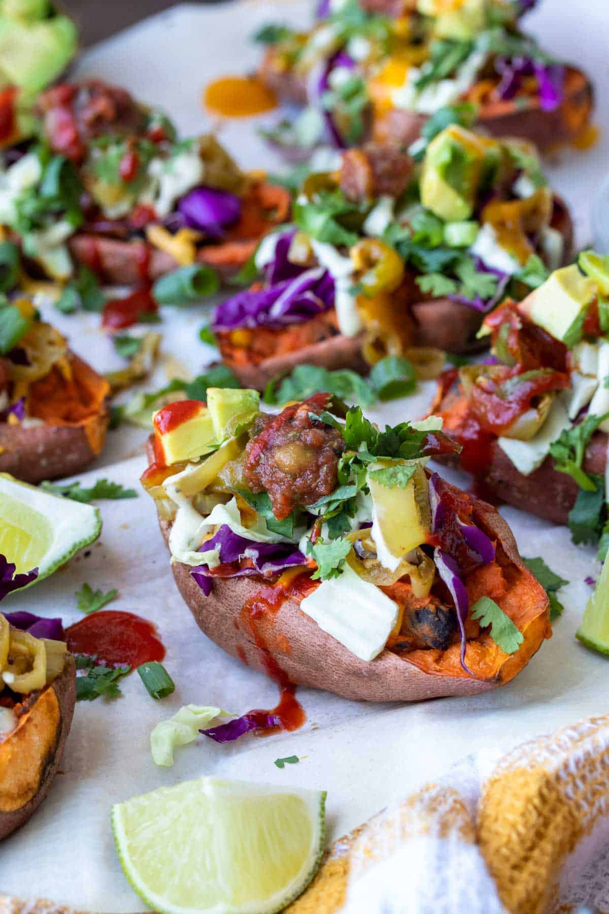 Front view of sweet potato skin loaded with toppings on white parchment