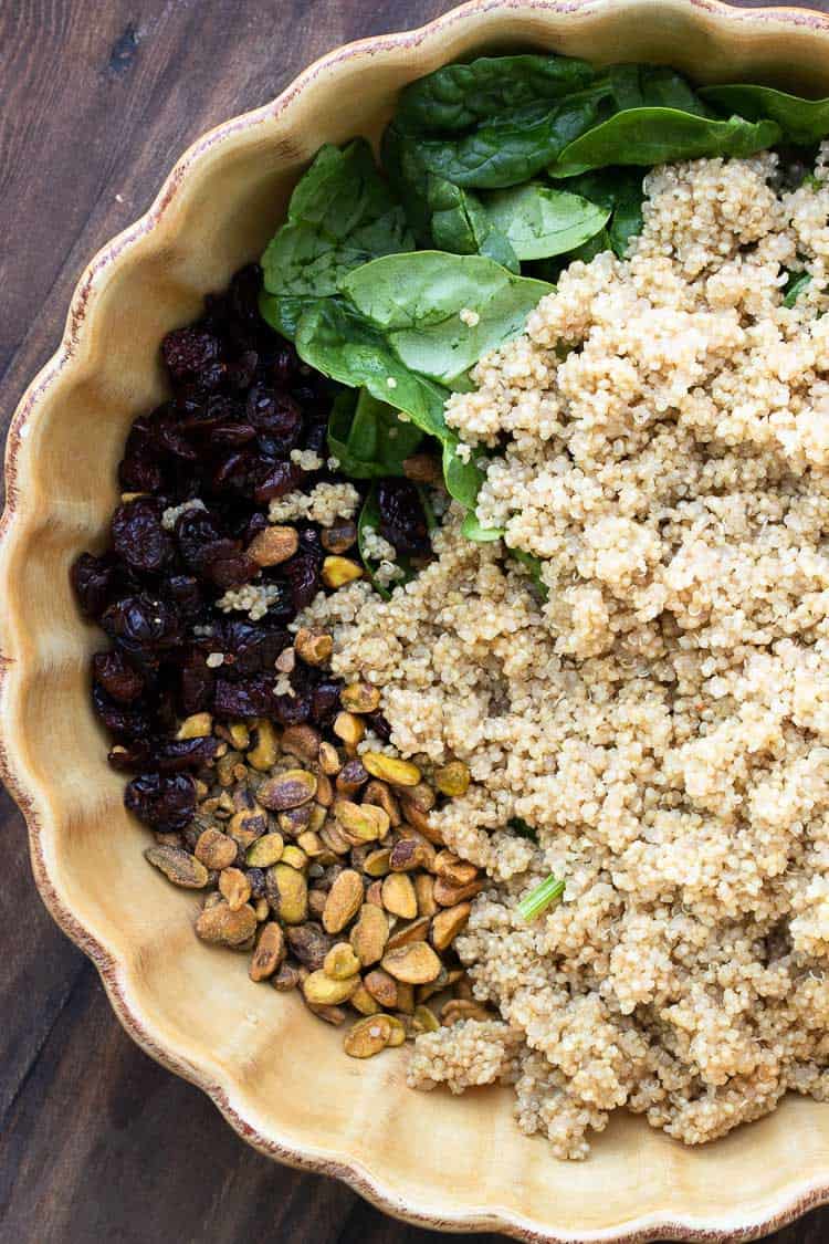 Top view of cranberries, pistachios, spinach and quinoa in a yellow bowl