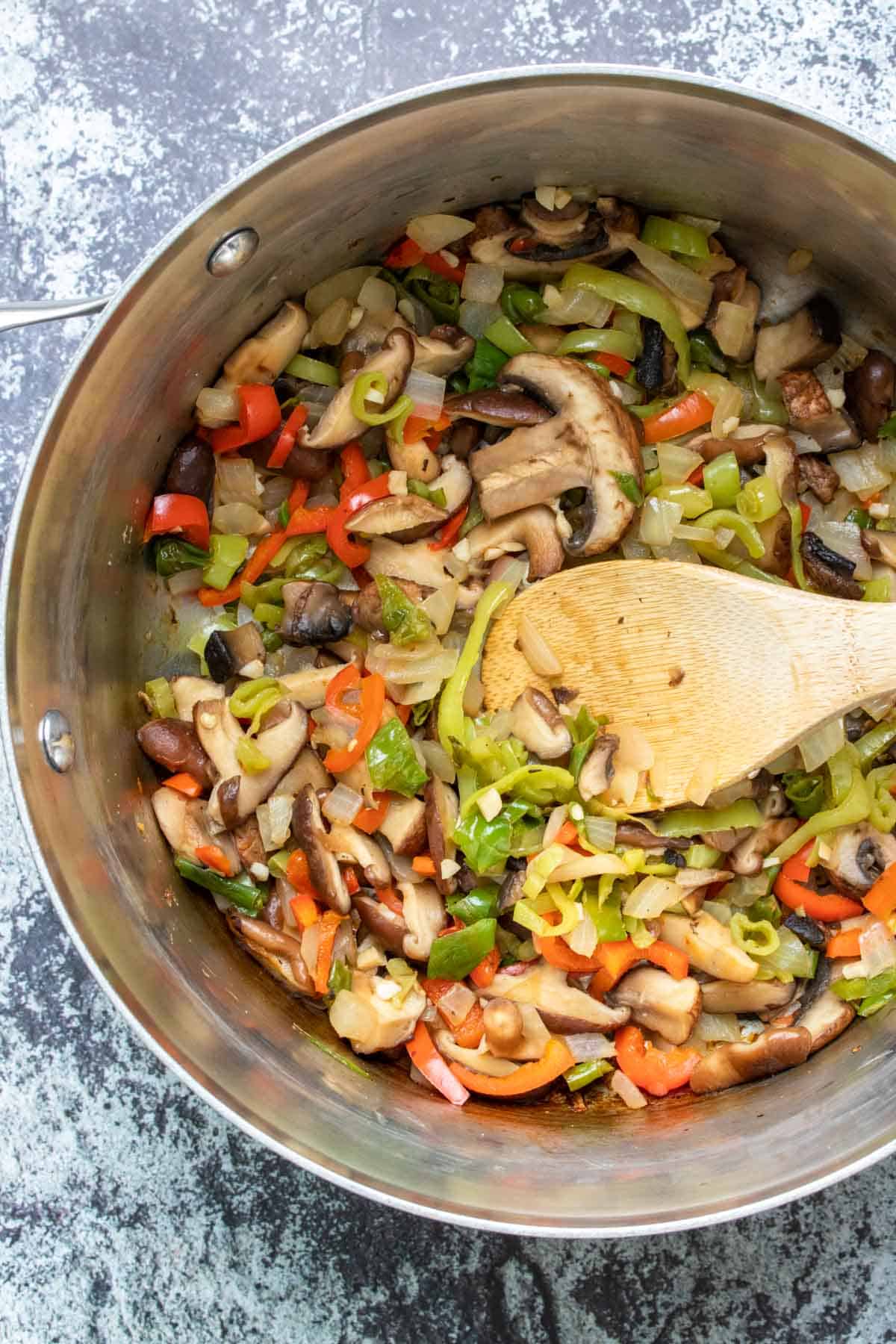 Wooden spoon stirring mixed veggies in a silver pot