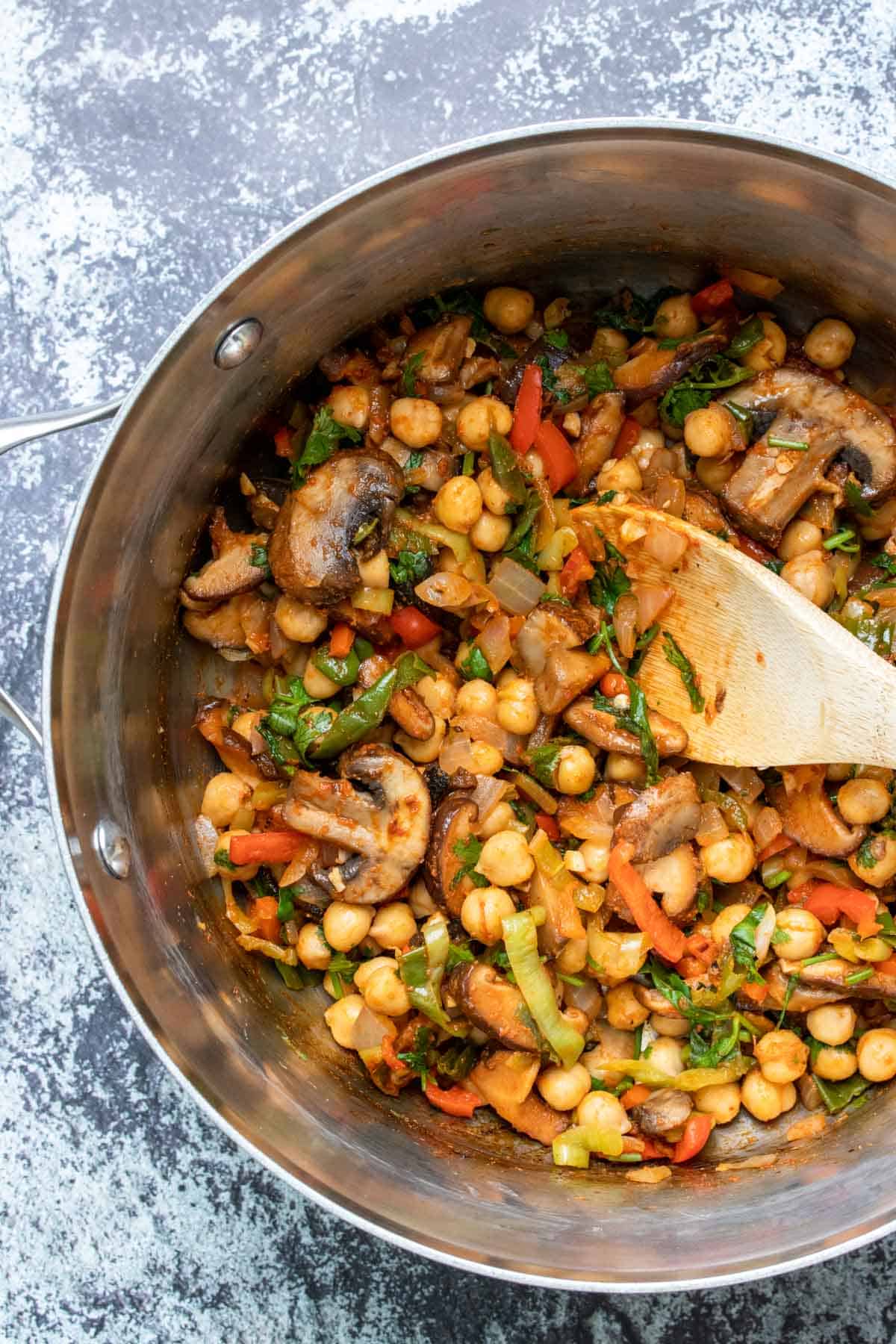 Wooden spoon stirring mixed veggies with red seasoning in a pot