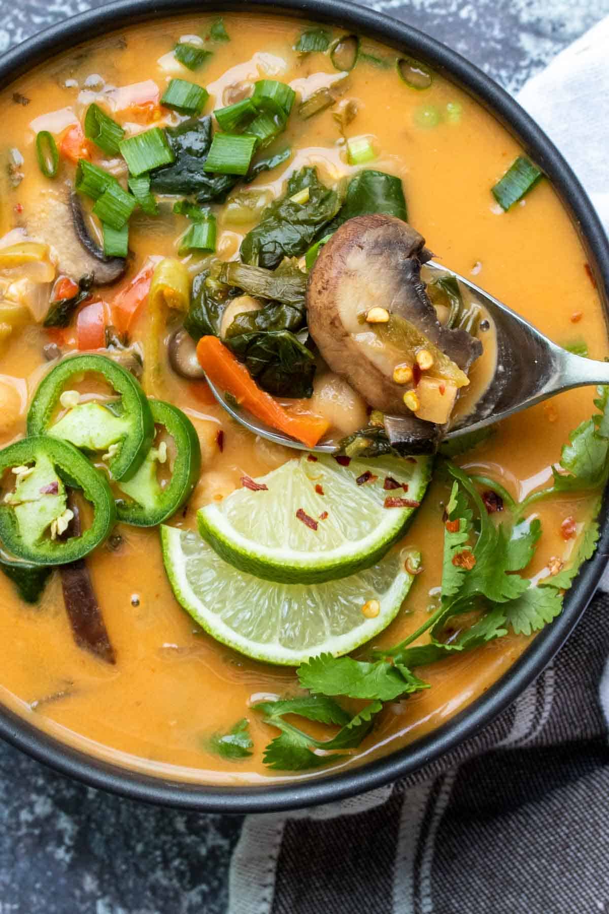 Cucchiaio che raccoglie un boccone di zuppa al curry di cocco con verdure