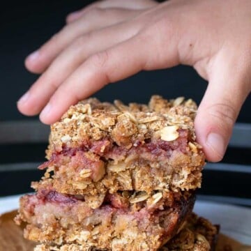 Child's hand taking a cranberry crumble bar off of a stack