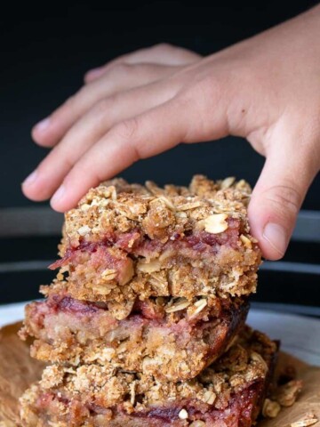 Child's hand taking a cranberry crumble bar off of a stack