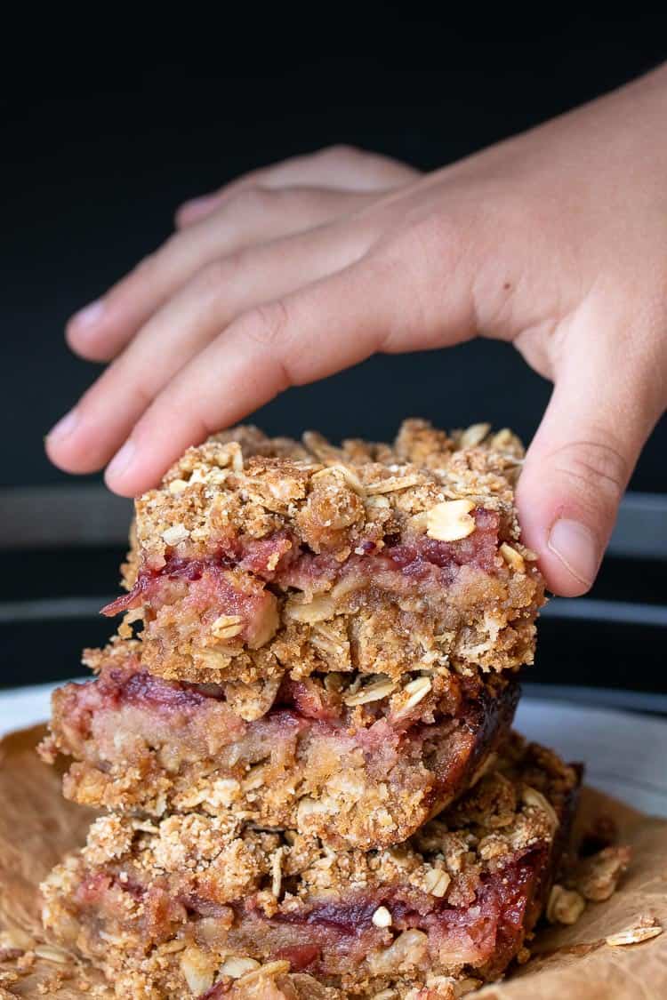 Child's hand taking a cranberry crumble bar off of a stack