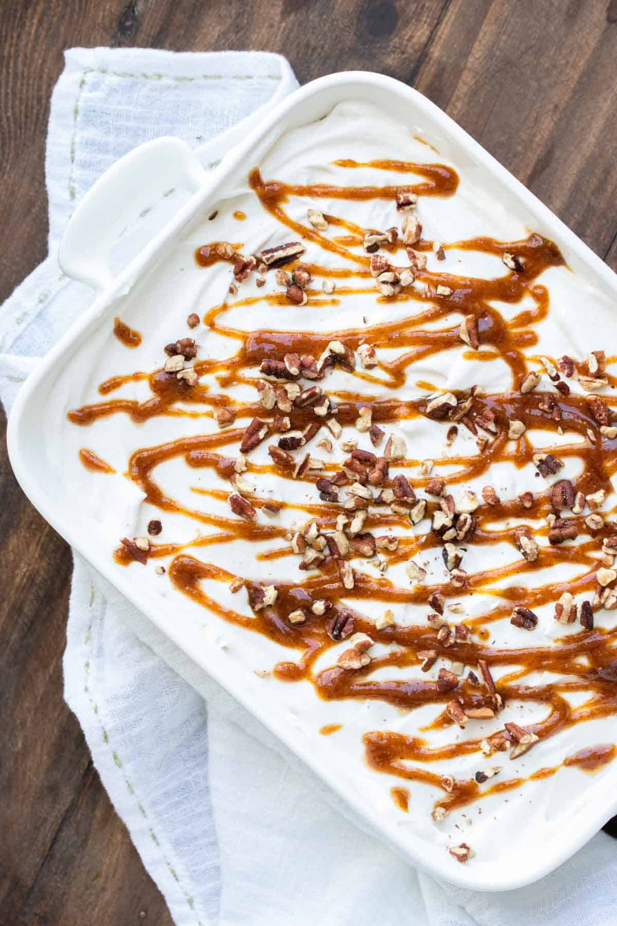Top view of white baking dish with whipped topping topped with pecans and caramel.