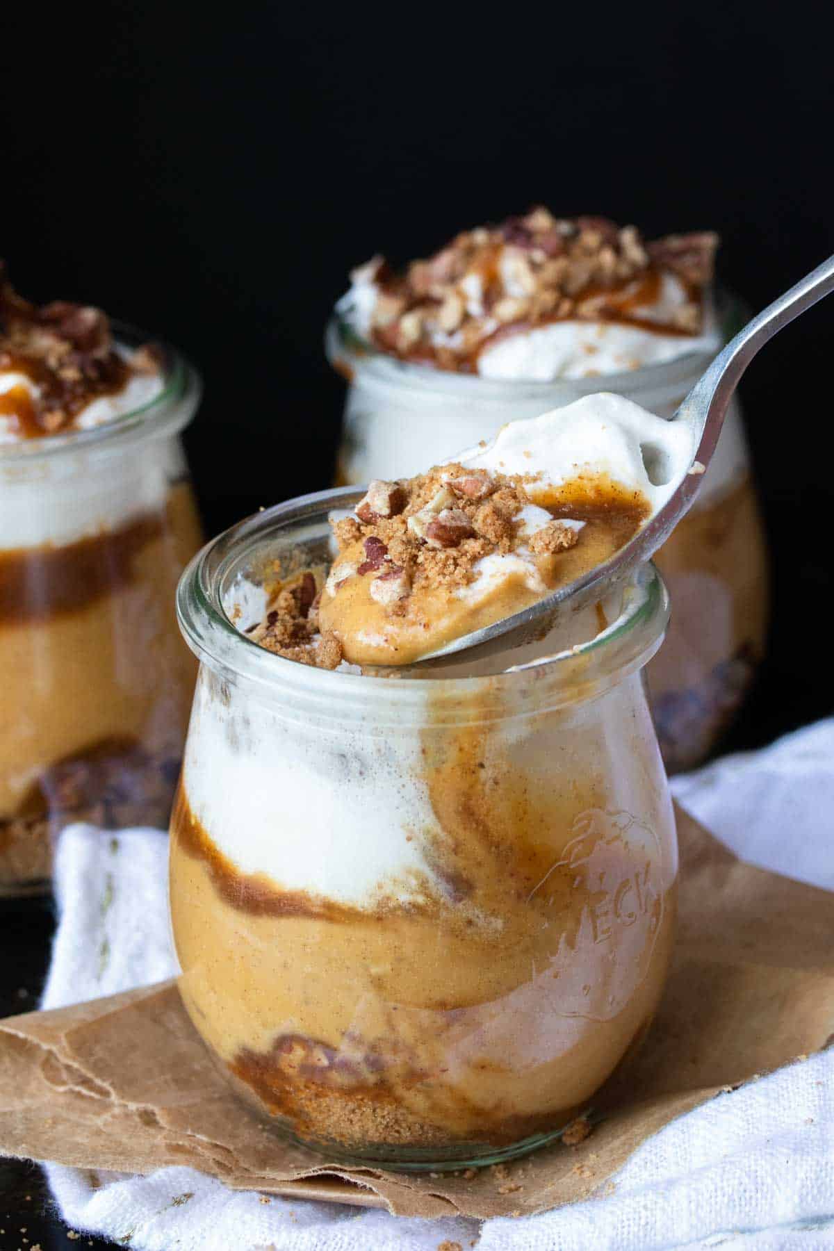 Spoon scooping a bite of creamy pumpkin dessert out of a glass jar.