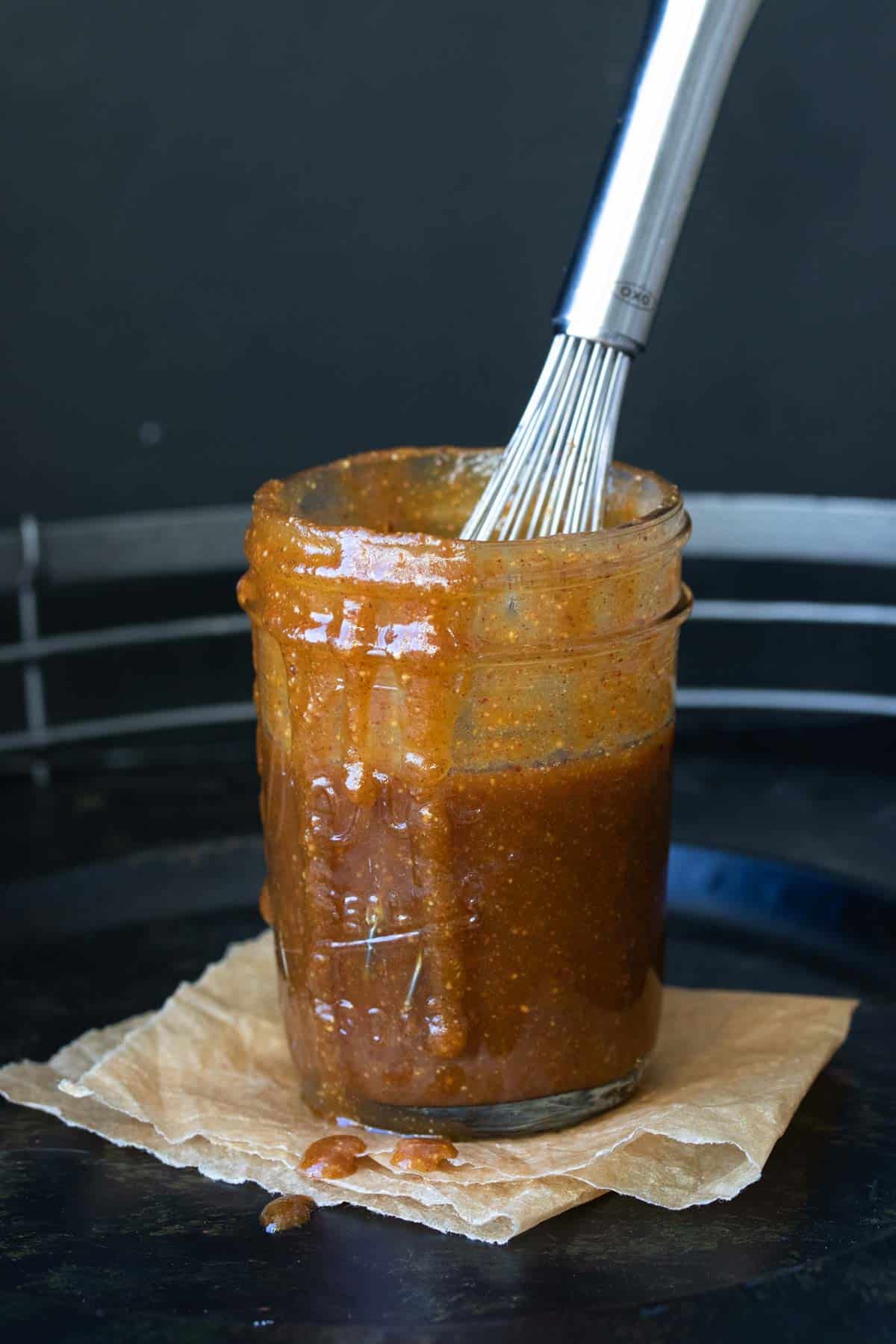 Whisk in a glass jar mixing a brown orange pumpkin caramel sauce.