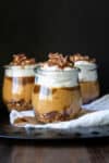 Three glass jars layered with cookies, pumpkin, caramel and whipped cream.