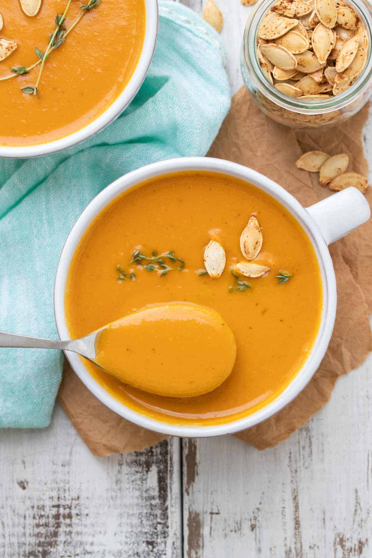 Top view of spoon scooping out butternut squash soup from a white soup mug.