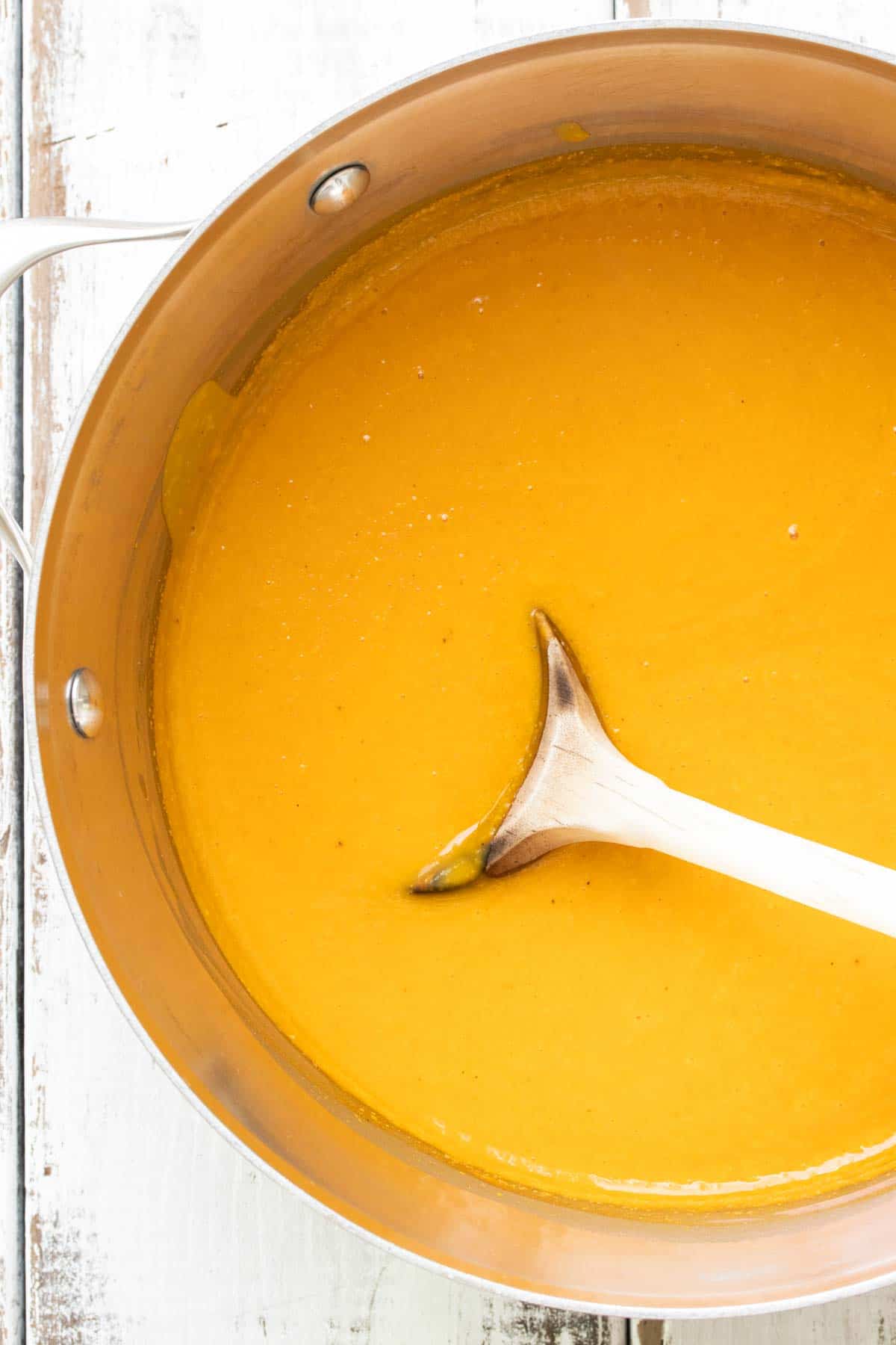 Wooden spoon mixing vegan butternut squash soup in a metal pot.