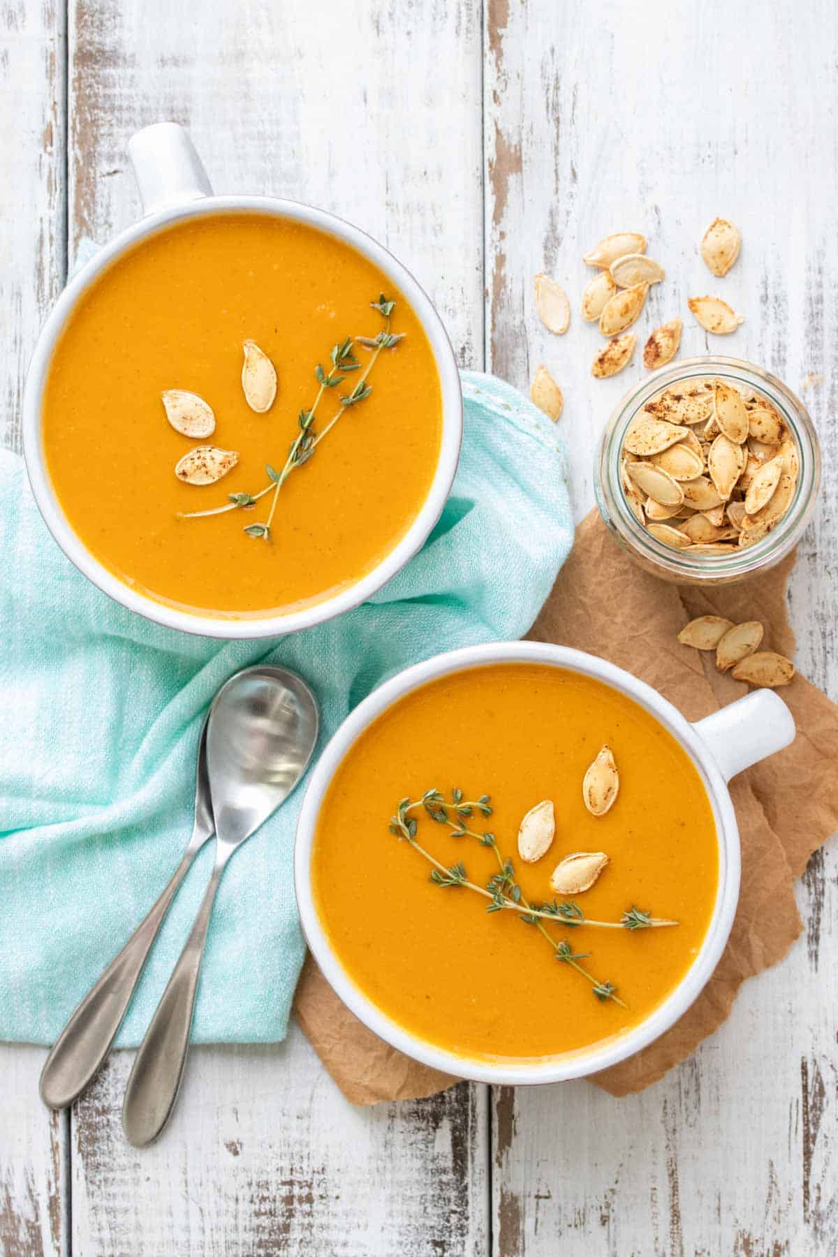 Top view of two soup mugs with butternut squash soup on a white wooden table