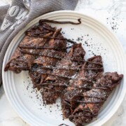 White plate with five chocolate cannoli drizzled in chocolate and powdered sugar