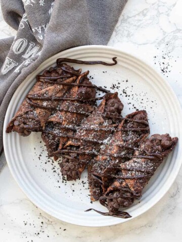 White plate with five chocolate cannoli drizzled in chocolate and powdered sugar