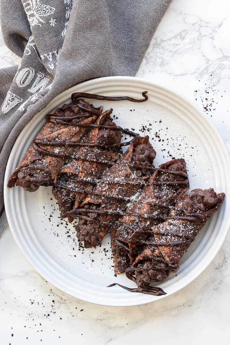 White plate with five chocolate cannoli drizzled in chocolate and powdered sugar