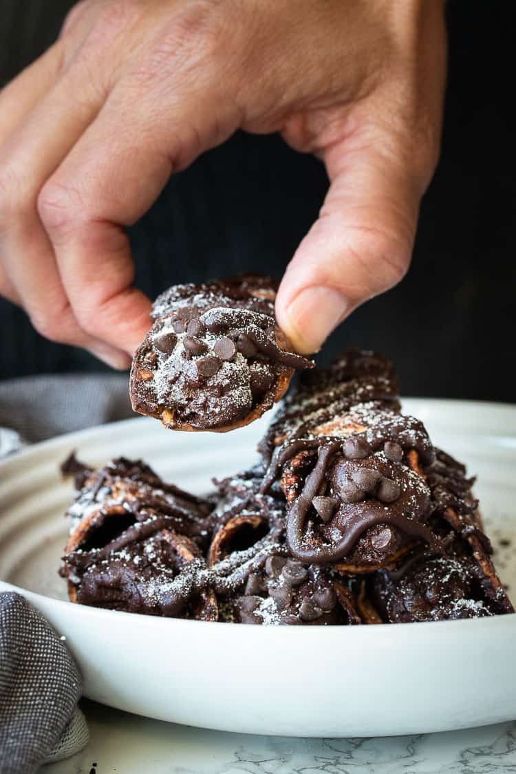 Hand picking up a chocolate cannoli off a pile in a white plate