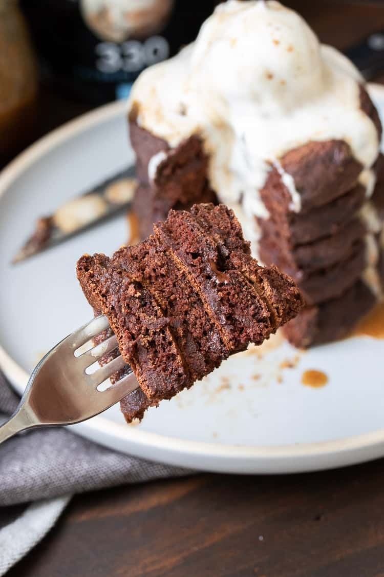 Fork filled with pieces of chocolate pancakes in front of a plate with a pancake stack