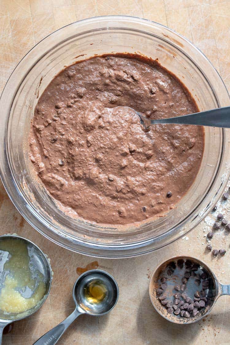 Glass bowl filled with chocolate pancake batter being mixed with a metal spoon