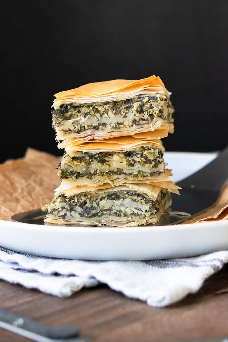 White plate with three pieces of Greek spanakopita piled on top