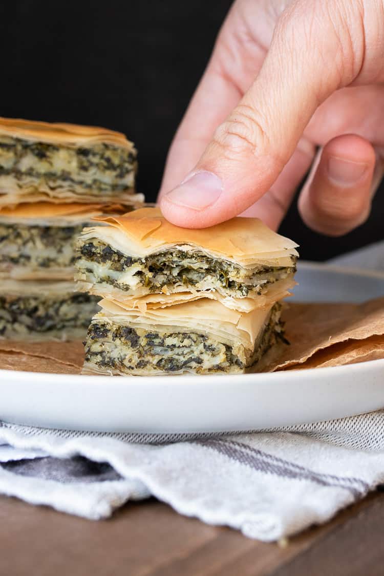 Hand picking up a piece of spanakopita with a bite out of it