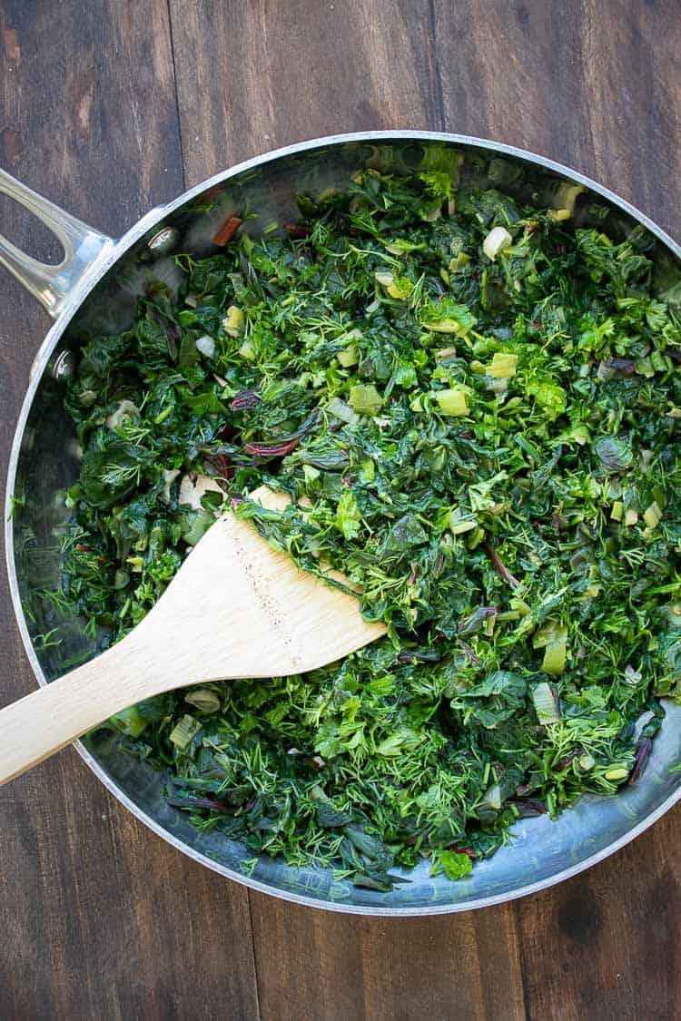 Chopped greens and herbs being sautéed in a metal pan