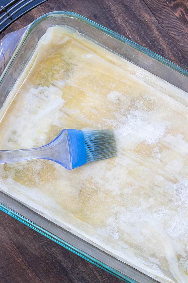 Blue pastry brush brushing olive oil on a phyllo (filo) pastry sheet