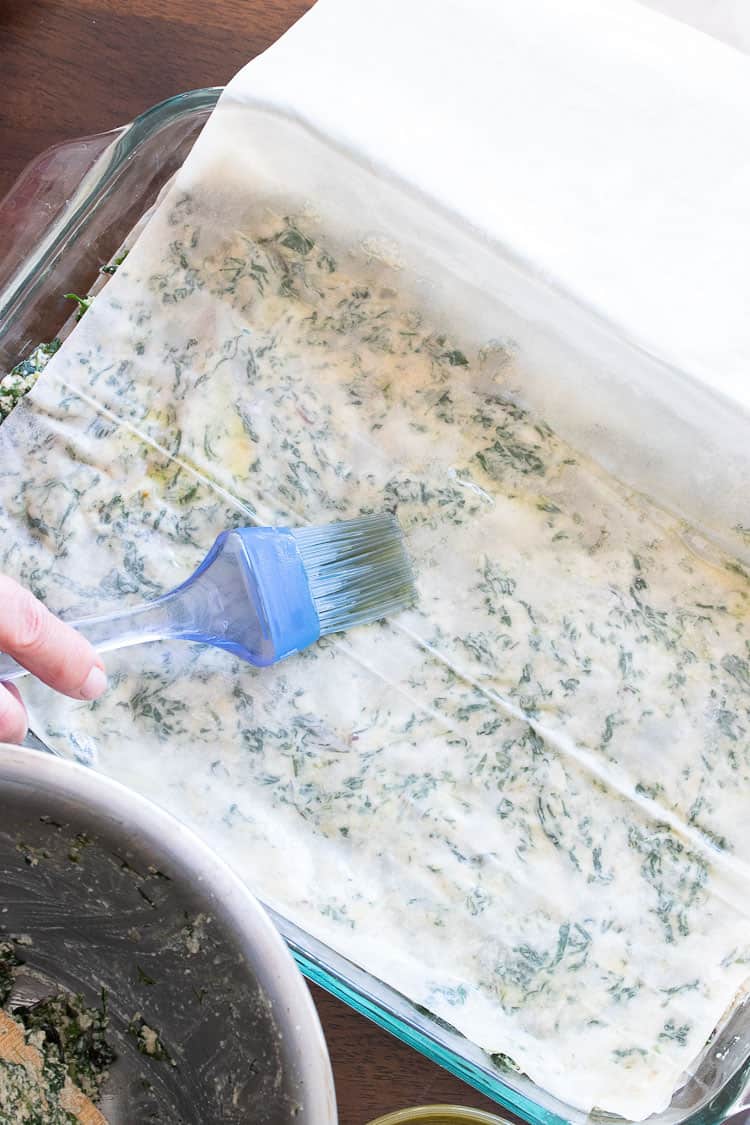 Spanakopita being constructed with layered phyllo (filo) sheets in a glass baking dish