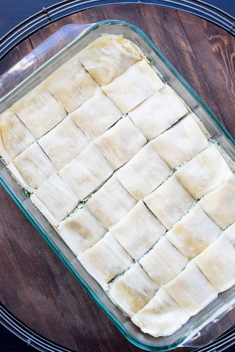 Cut squares of unbaked spanakopita in a glass baking dish
