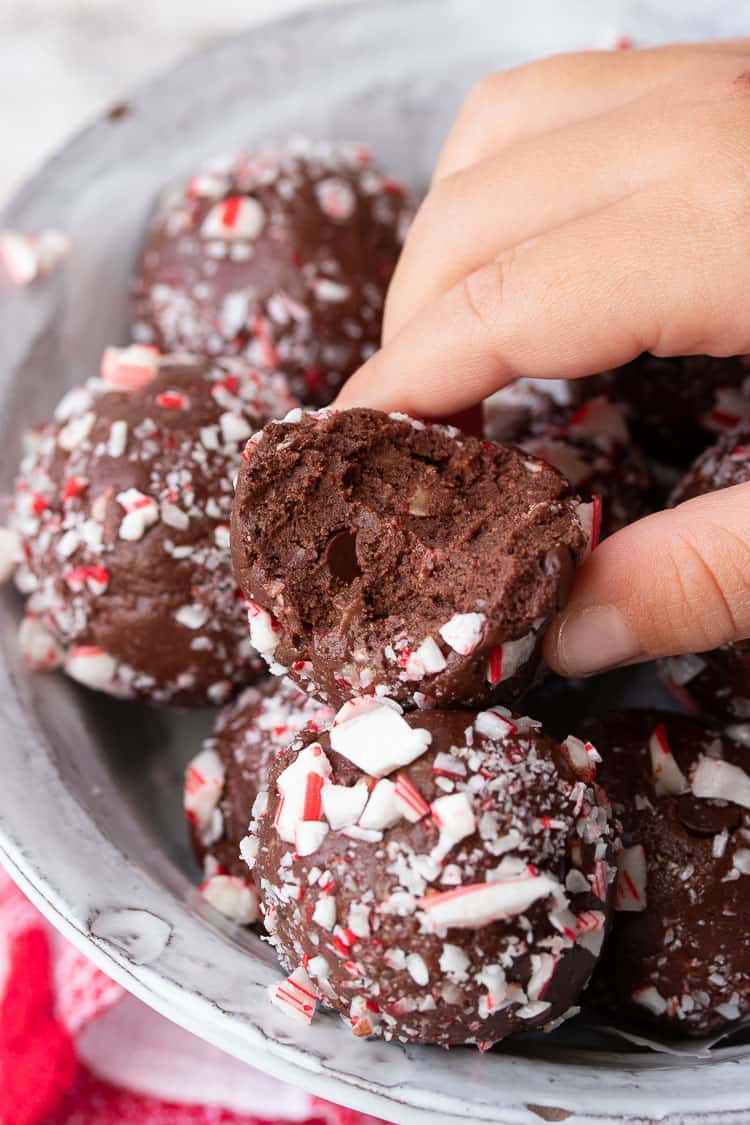 Fingers grabbing a chocolate peppermint candy cane ball with a bite out of it