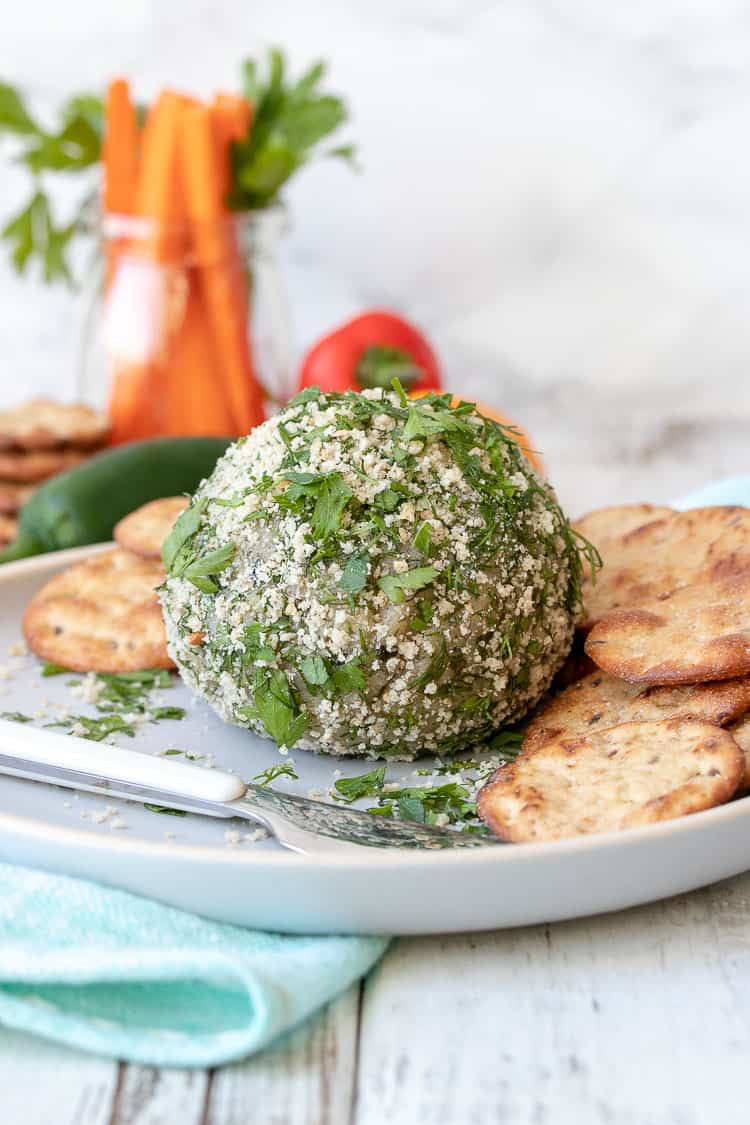 Breadcrumb and herb coated cheese ball on a white plate next to crackers