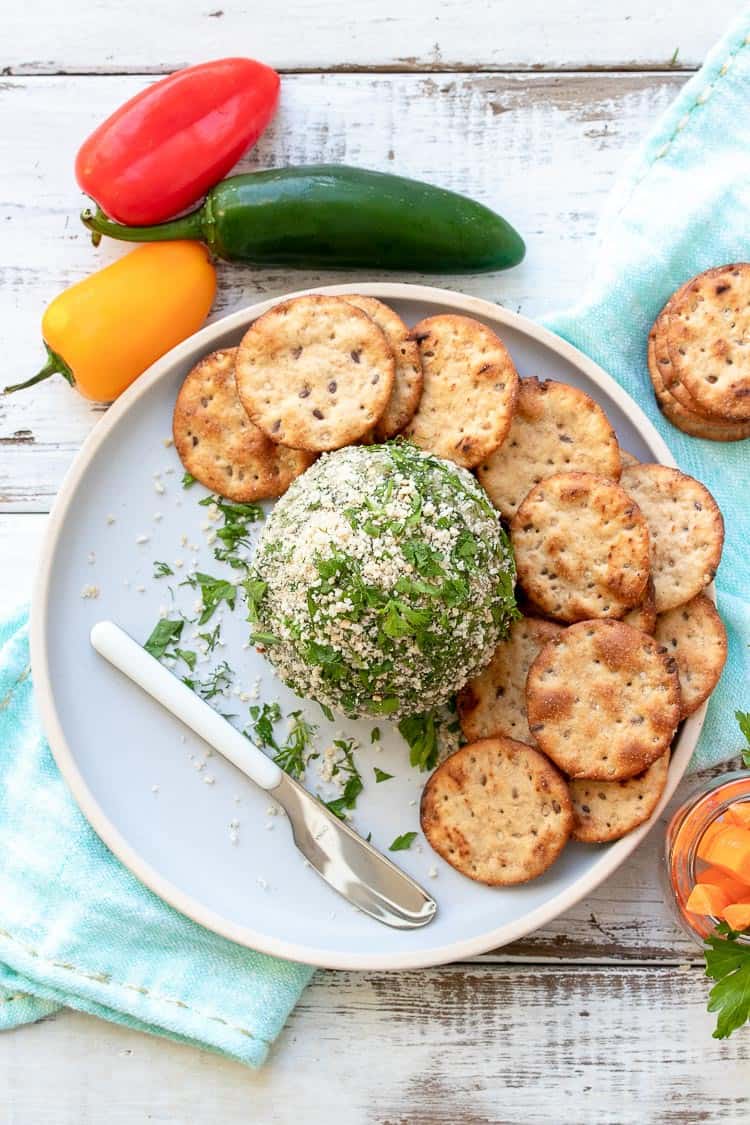 Top view of cheese ball on a grey plate surrounded by crackers, peppers and carrot sticks