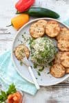 Grey plate with a knife with cheese ball spread on a round cracker