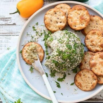 Grey plate with a knife with cheese ball spread on a round cracker