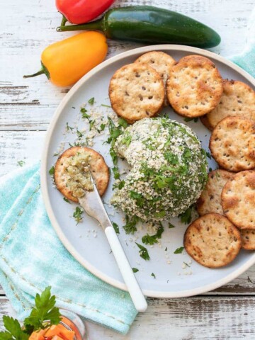 Grey plate with a knife with cheese ball spread on a round cracker