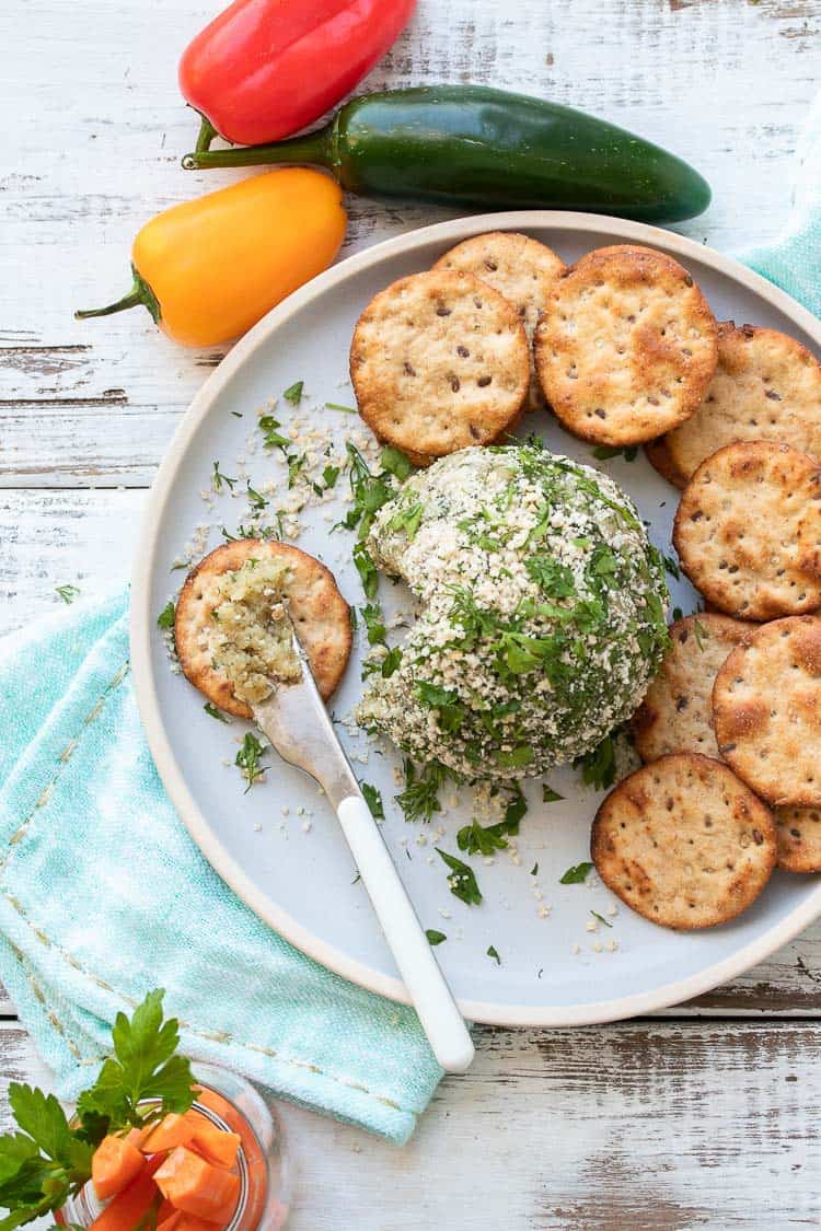 Grey plate with a knife with cheese ball spread on a round cracker 