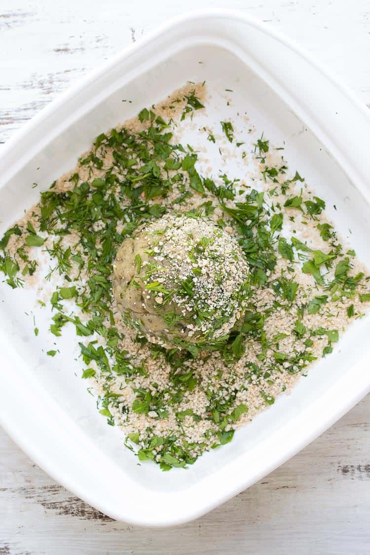 Top view of cheese ball being coated with breadcrumbs and chopped herbs