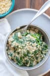 Top view of a grey bowl with a savory spinach oats in it and a spoon getting a bite from the bowl.