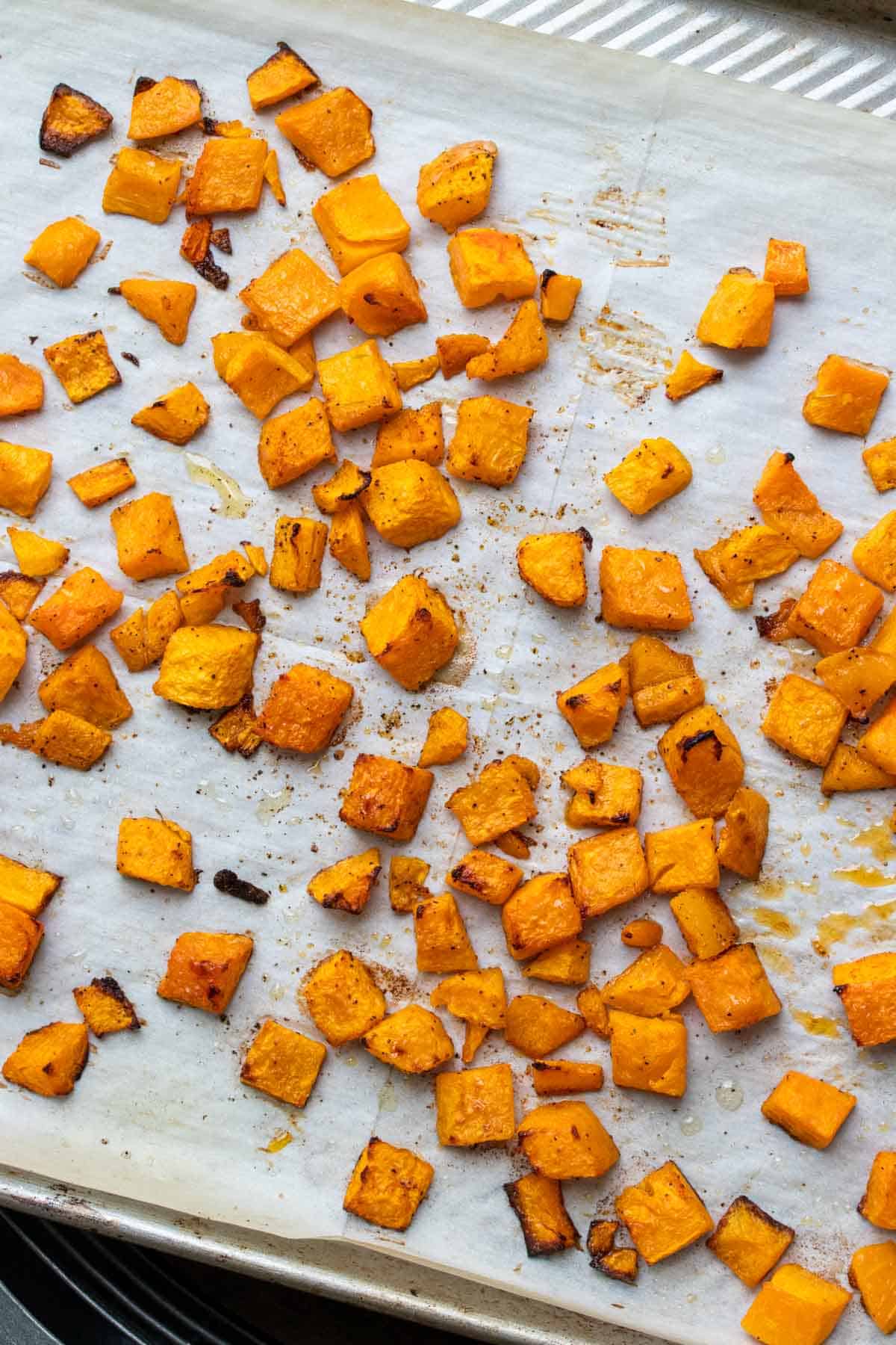 Cookie sheet with parchment paper filled with roasted pieces of butternut squash
