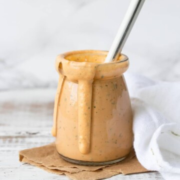Glass jar on a white wood table filled with a creamy orange sauce drizzling down the side