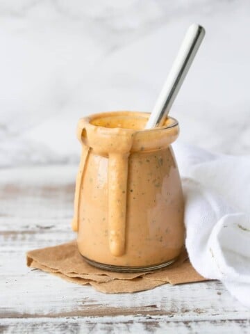 Glass jar on a white wood table filled with a creamy orange sauce drizzling down the side