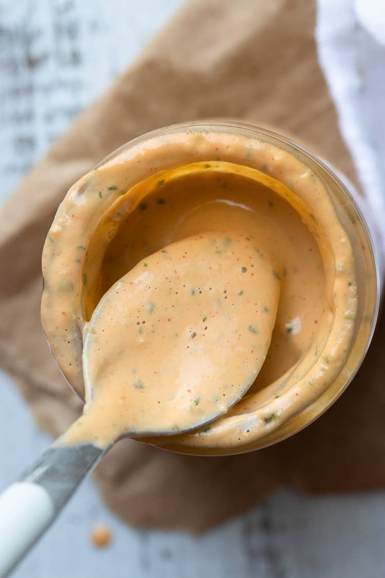 Spoon dipping into jar with a creamy orange sauce with green specks