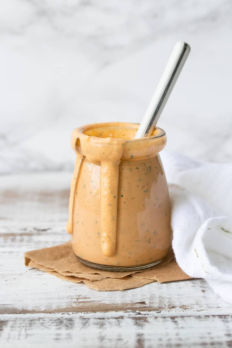 Glass jar on a white wood table filled with a creamy orange sauce drizzling down the side