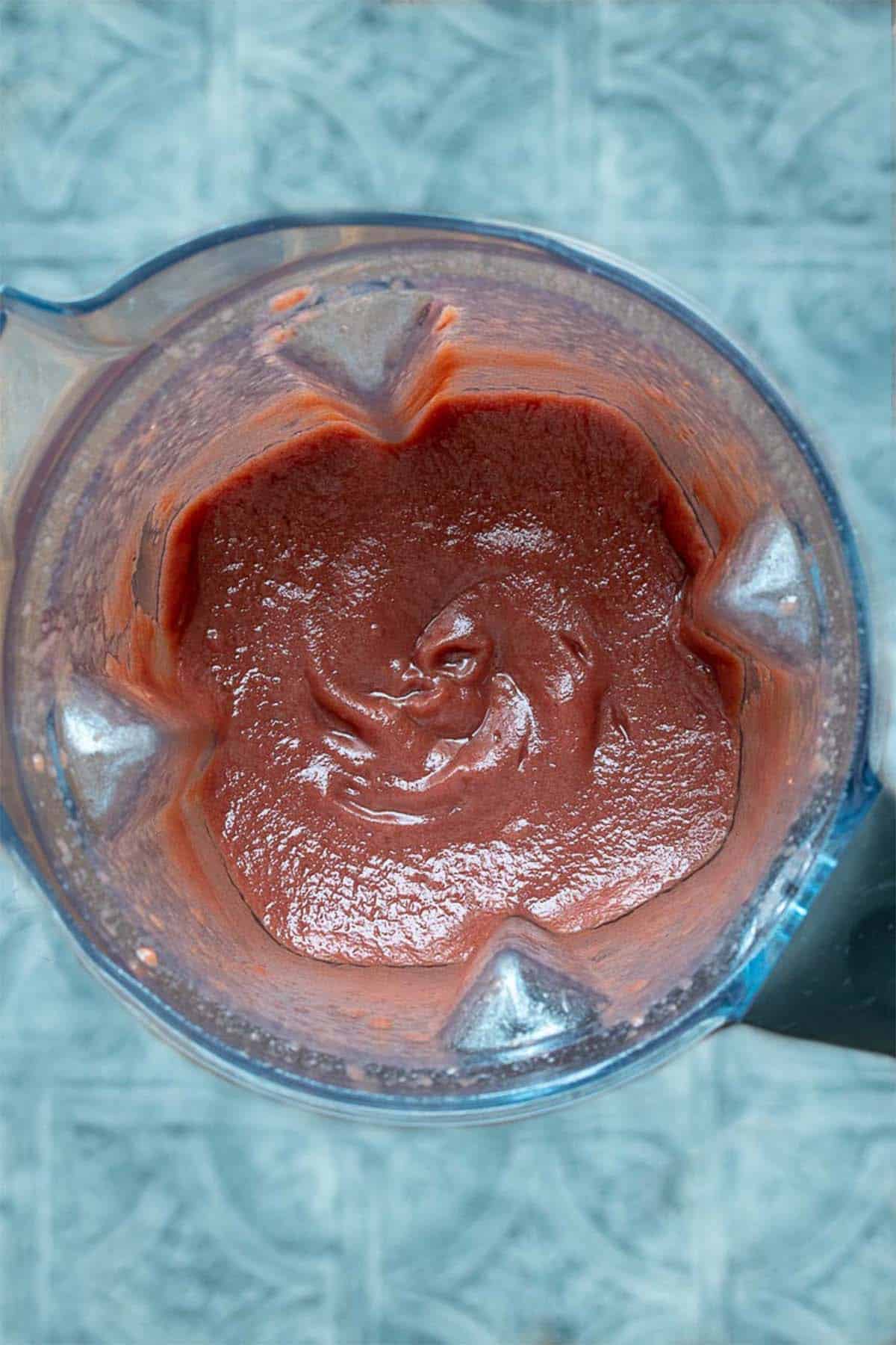 Top view of blender filled with strawberry puree on a blue surface