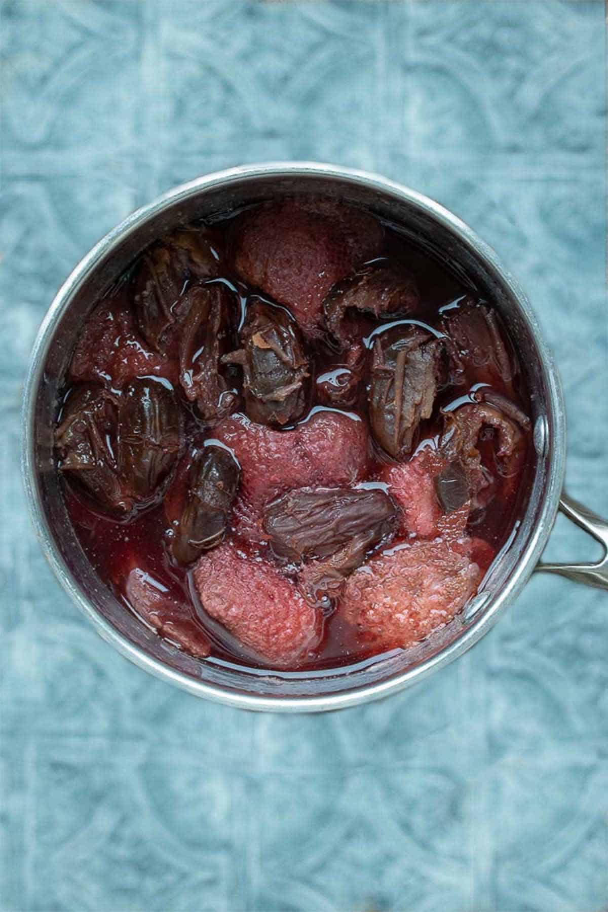 Metal pot filled with strawberries, dates and water on a blue surface