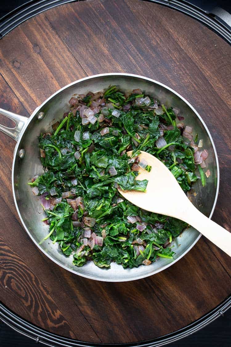 Top view of spinach and red onion sauteed in a frying pan