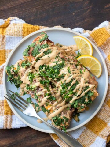 Two spinach and chickpea enchiladas on a grey plate with creamy drizzle on top