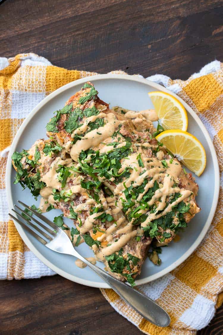 Two spinach and chickpea enchiladas on a grey plate with creamy drizzle on top