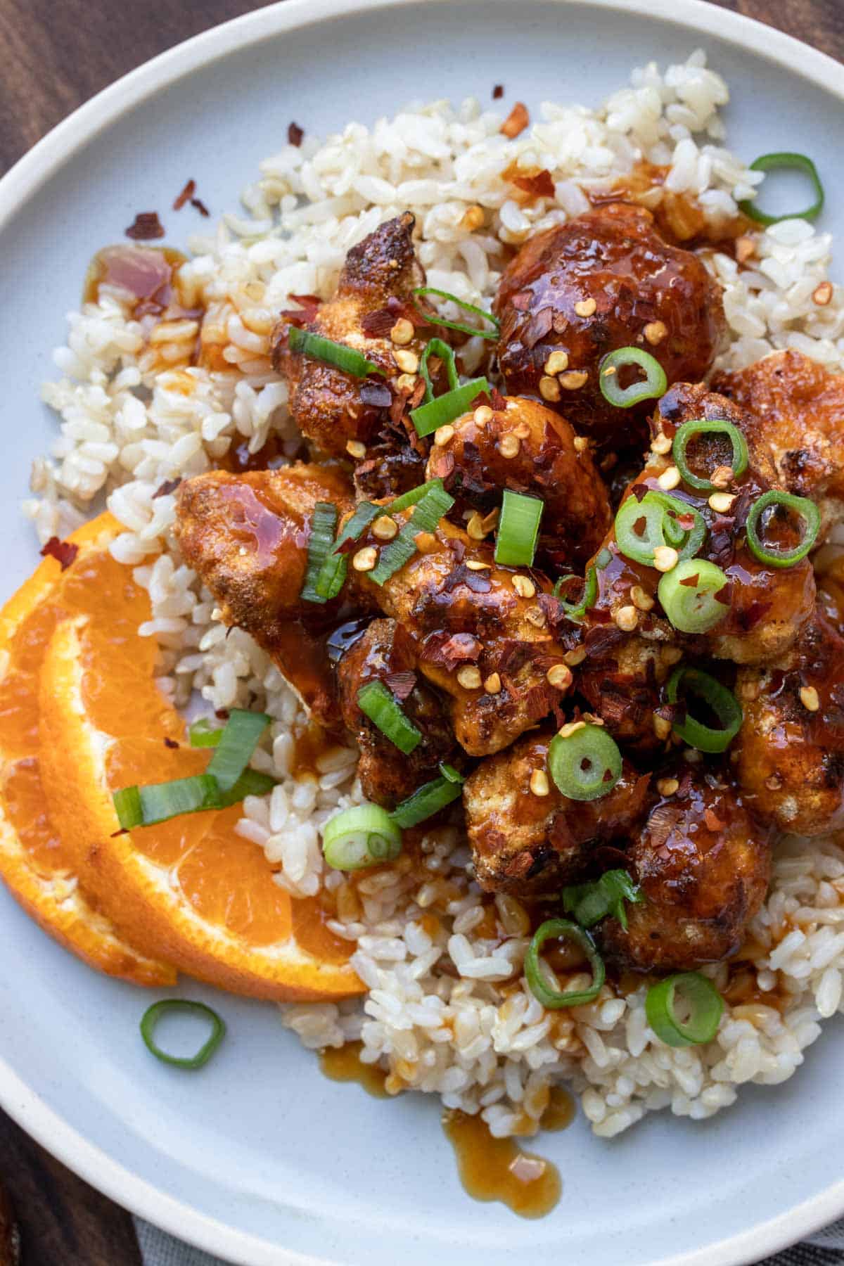 Close up of crispy cauliflower tossed in Chinese orange sauce over rice