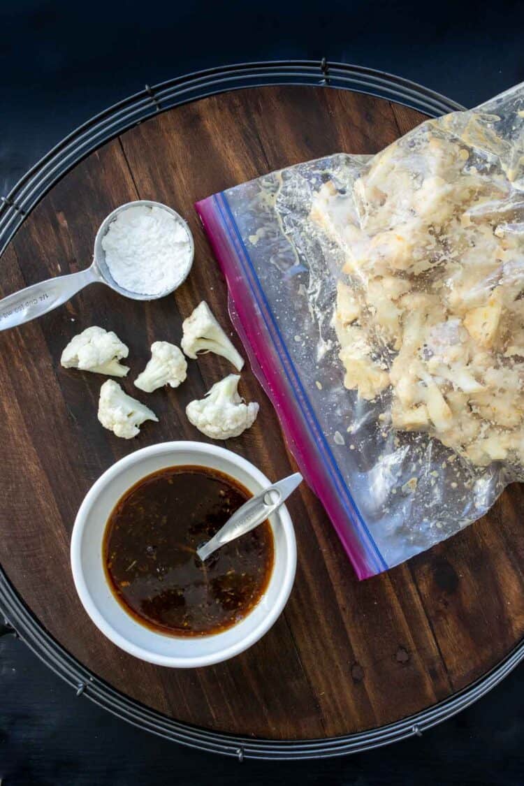Plastic bag filled with cauliflower pieces next to bowl with brown sauce