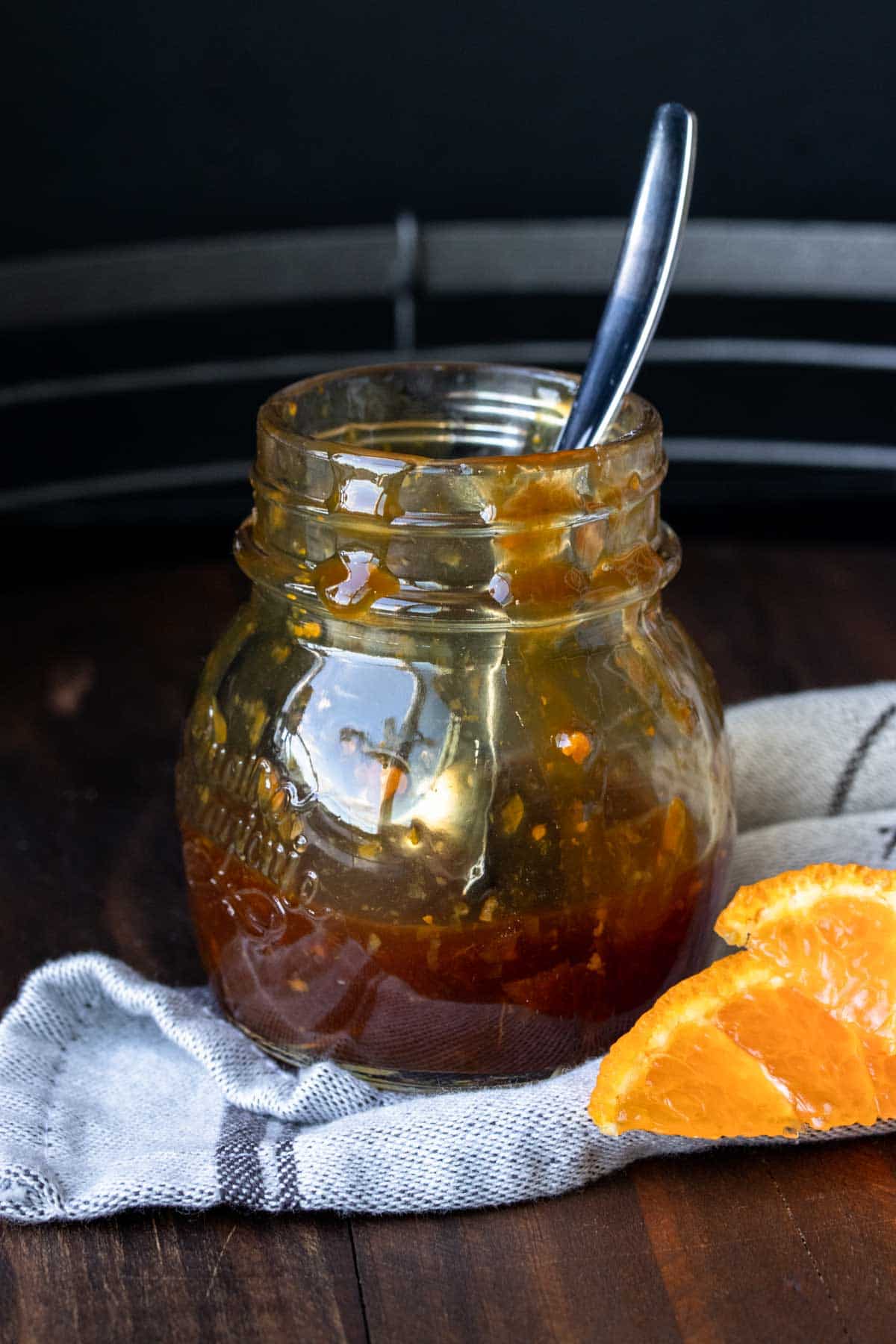 Glass jar with spoon inside filled with brown orange sauce on a grey napkin