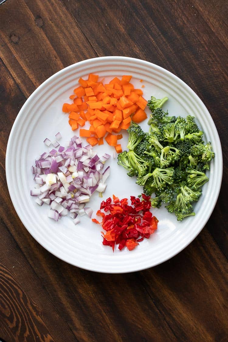 White plate with chopped carrots, broccoli, red peppers and red onions